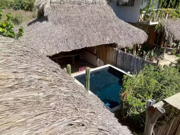 Uma construção com telhado de palha, piscina e vegetação ao redor.