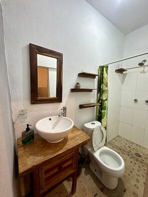 Casa de banho com toucador de madeira, uma sanita, chuveiro e lavatório branco.