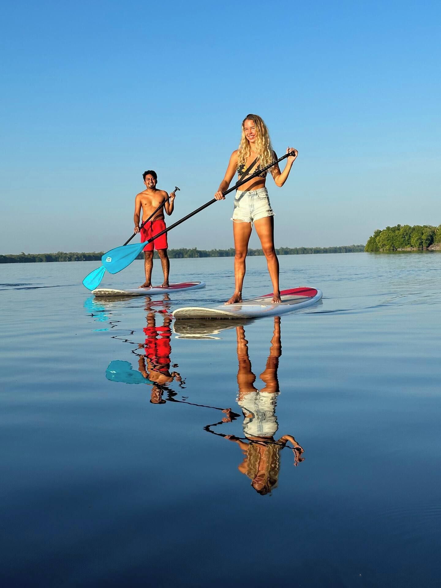 Twee personen op paddleboards op kalm water, met zichtbare reflecties.