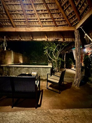 Un espace extérieur aménagé avec des meubles en osier, un comptoir de bar et une structure dotée d’un toit de chaume.