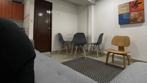 Un soggiorno con un divano grigio, una sedia di legno e una sedia nera. Si nota una porta e una parete con un quadro.