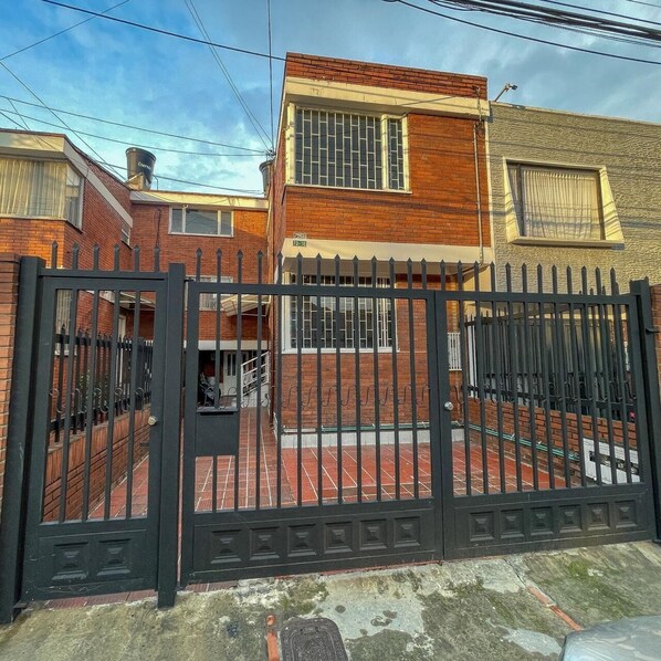 Área residencial murada com casas de tijolo, um portão visível e céu claro.