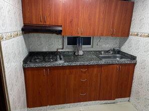 A kitchen with wooden cabinets, a gas stove, a sink, and a microwave. - Apartment near the airport, modern shopping malls and entertainment centers (Bogotá)