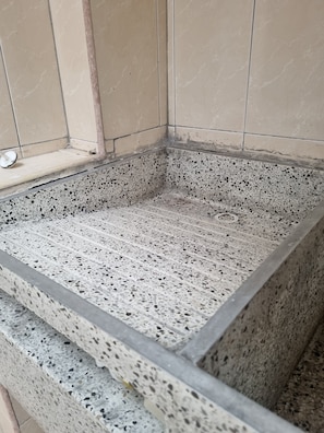 Um canto de um quarto com piso de terrazzo e paredes revestidas de azulejos.