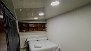 A bedroom with a bed, a wooden chair, a shelf with decorative items, and a window with blinds. - Apartment near the airport, modern shopping malls and entertainment centers (Bogotá)