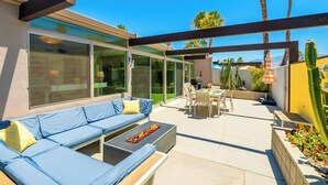 Eine Terrasse mit einer blauen Couch, einer Feuerstelle und einem Essbereich mit Stühlen und Tisch.