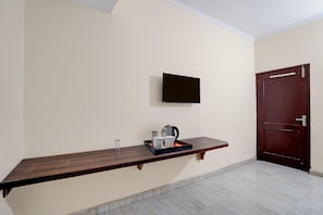 A room with a wooden bench, a flat-screen TV mounted on the wall, a door, and a tiled floor. - Classic Global Tower (Mathura)