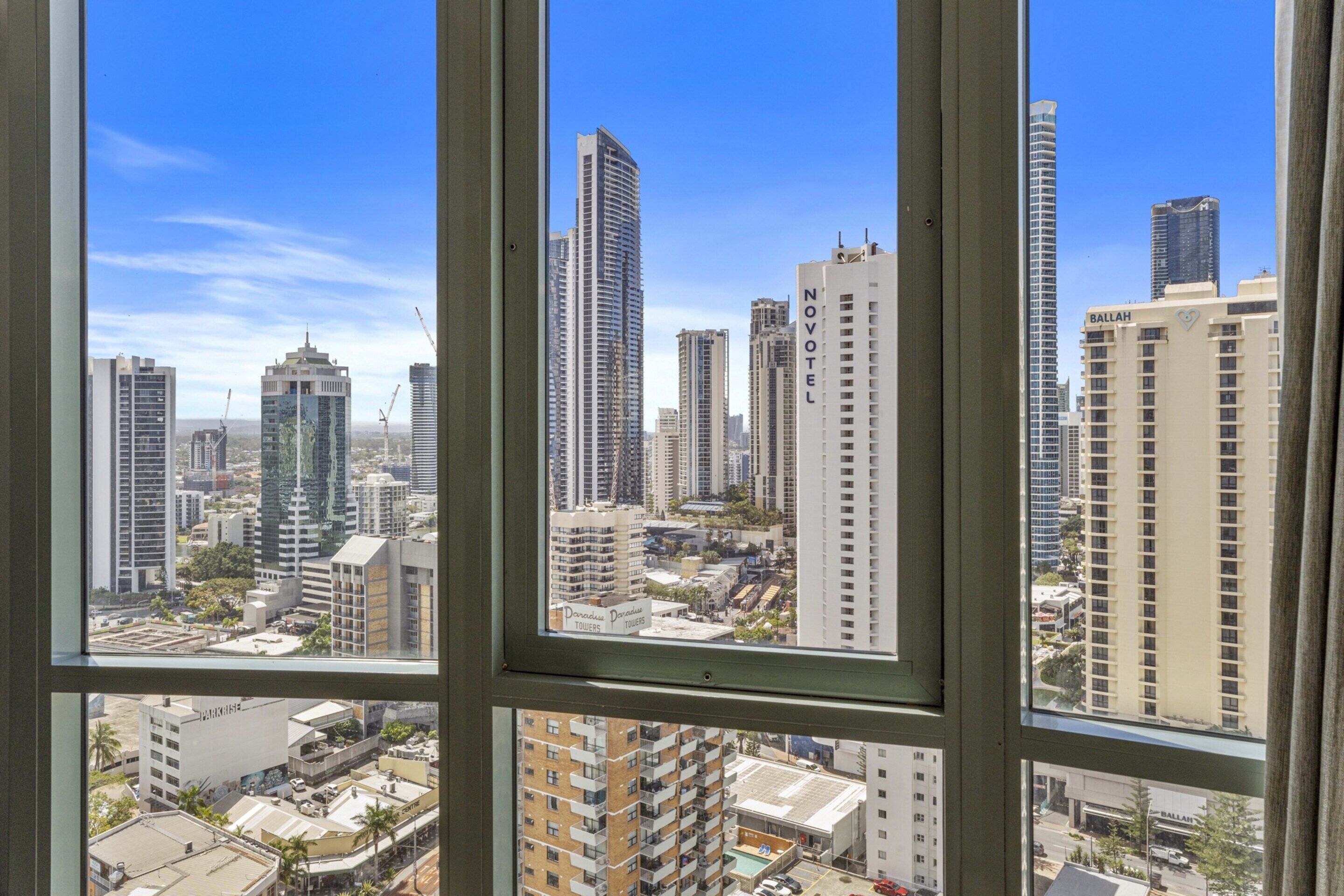 A cityscape through a window with high-rise buildings, including a Novotel hotel.