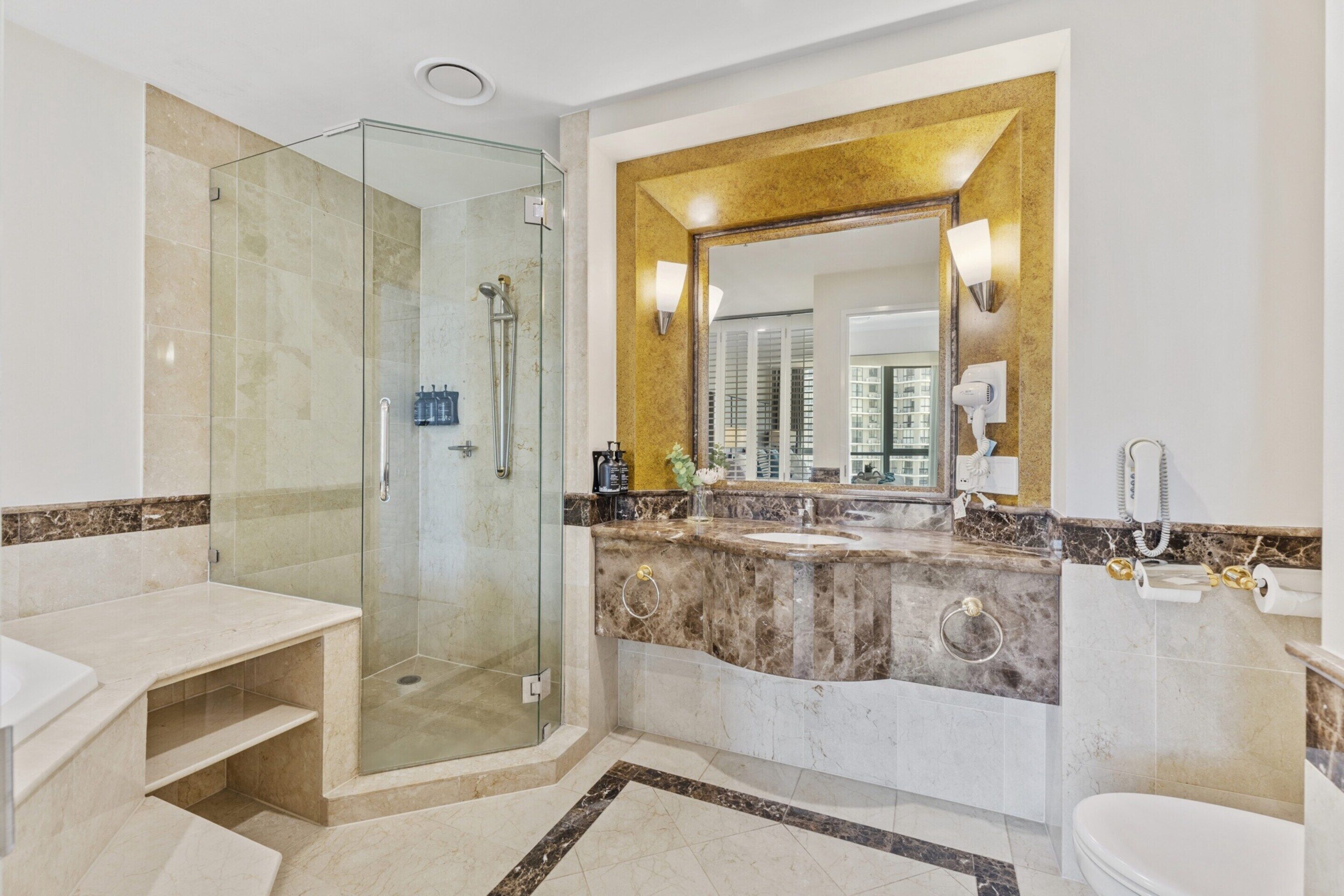 A modern bathroom with a glass-enclosed shower, a large mirror, and a marble countertop.
