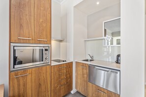 A compact kitchen with wooden cabinets, a built-in microwave, a stainless steel dishwasher, and a large mirror above the sink. - Bright Apartment Near Surfers Paradise Beach (Gold Coast)