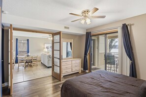 Ein Schlafzimmer mit Bett, Schminktisch, Deckenventilator und Blick auf einen Balkon.