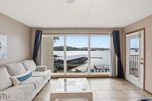 Ein Wohnzimmer mit einer Couch, einem Couchtisch und einem großen Fenster mit Blick auf einen Steg und Wasser.