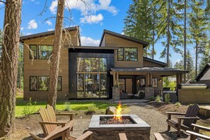 Ein modernes, zweistöckiges Haus mit Feuerstelle, Sitzgelegenheiten im Freien und einer Terrassenfläche.