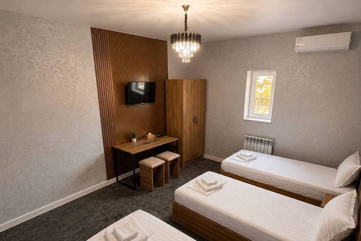 A hotel room with two beds, a desk, a TV, a chandelier, and a window.