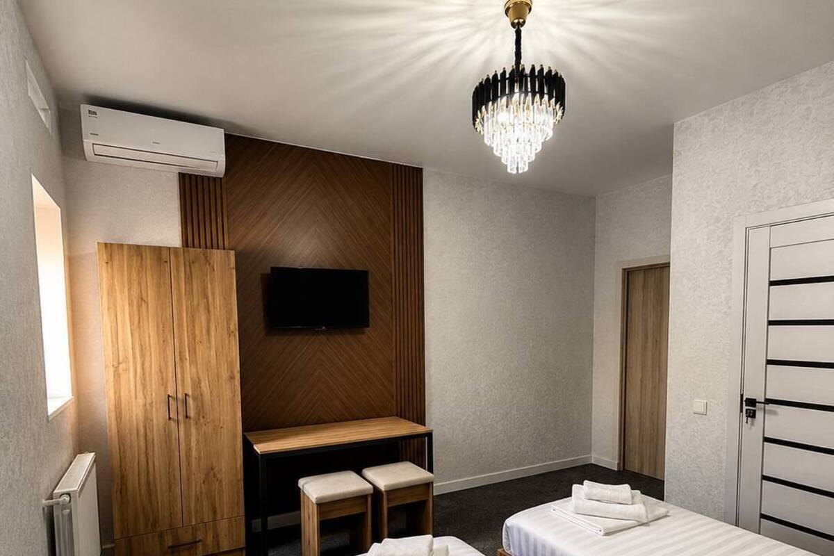 A hotel room with two beds, a desk, a TV, and a chandelier.