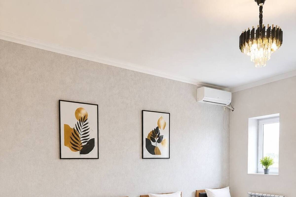 A hotel room with four single beds, a chandelier, artwork on the walls, and an air conditioning unit.