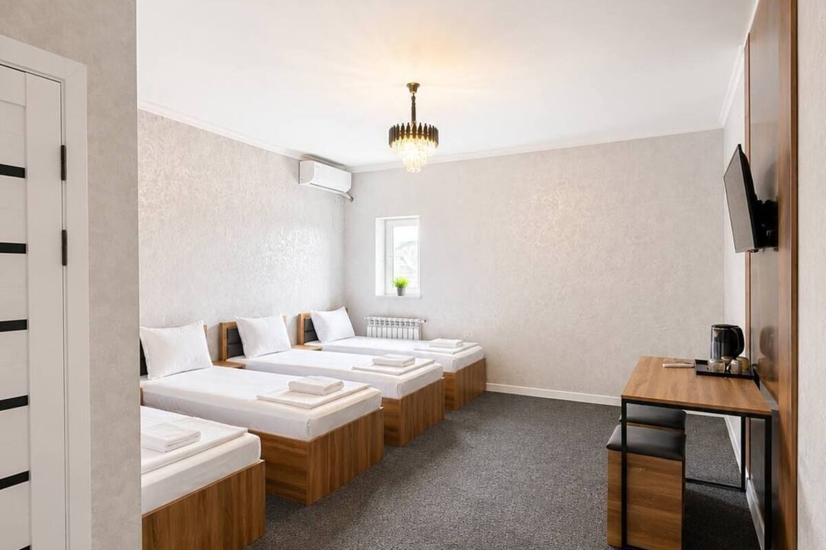 A hotel room with three beds, a desk, a TV, and a chandelier.