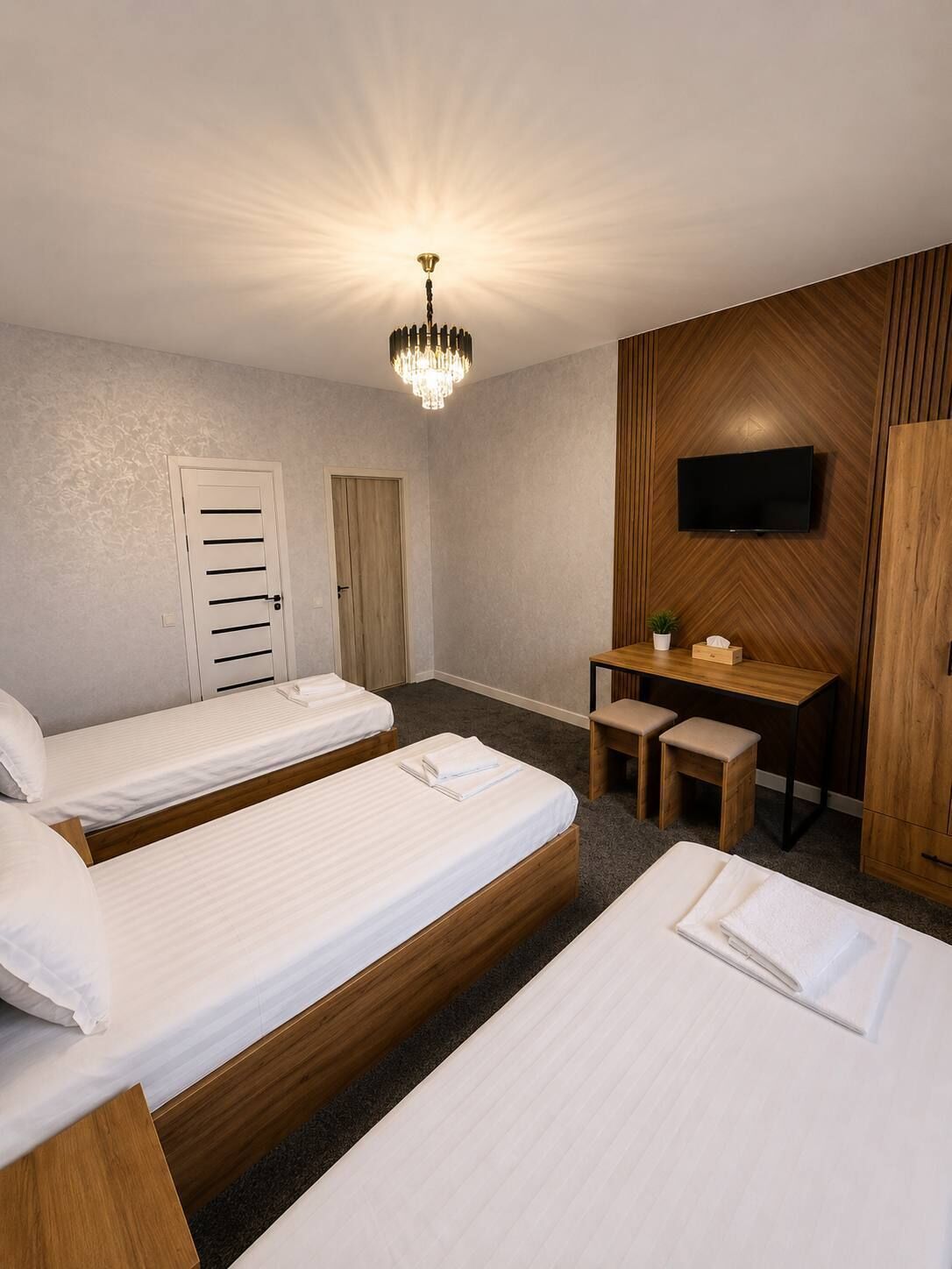 A hotel room with two beds, a desk, a television, and a chandelier.