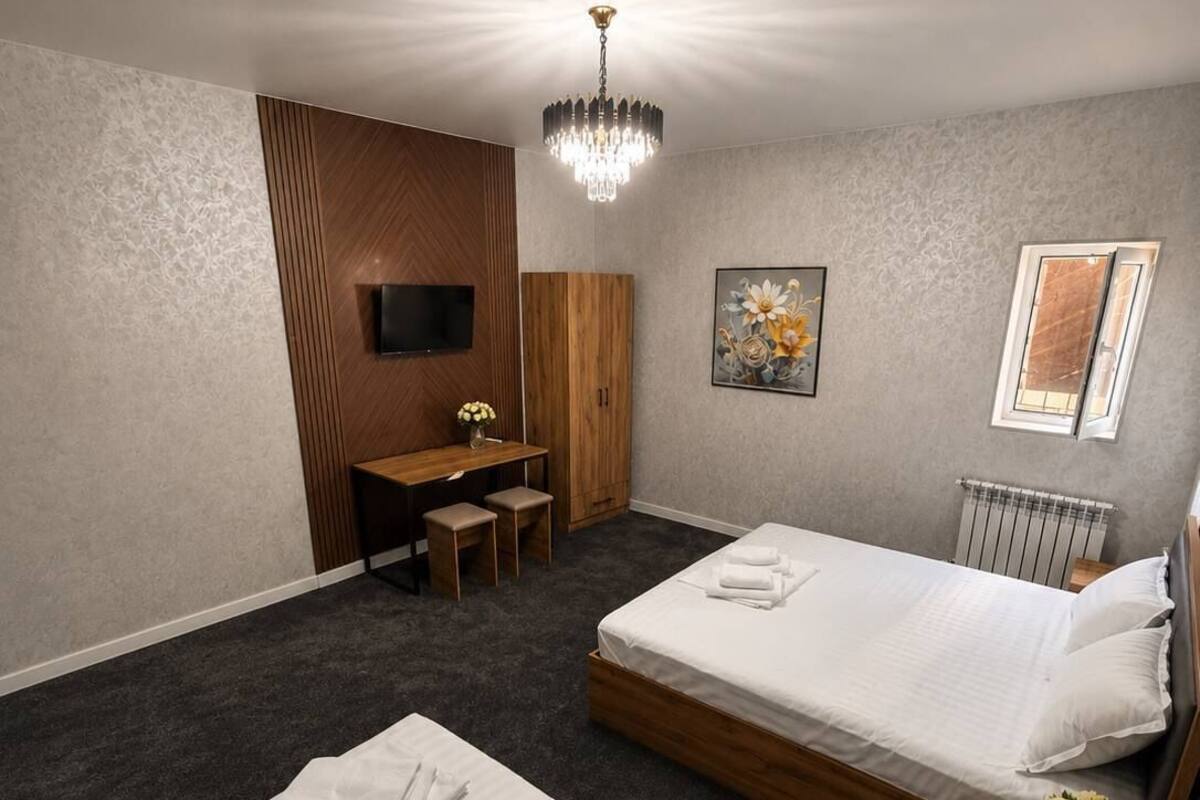 A hotel room with two beds, a desk, a TV, a chandelier, and a painting.