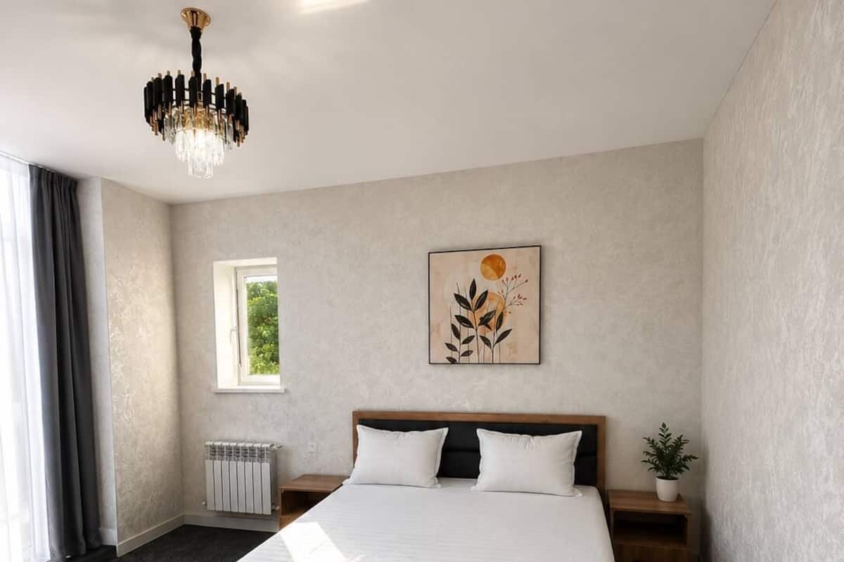 Une chambre dâhĂŽtel avec un grand lit, un lustre, une fenĂȘtre, un radiateur et une plante.