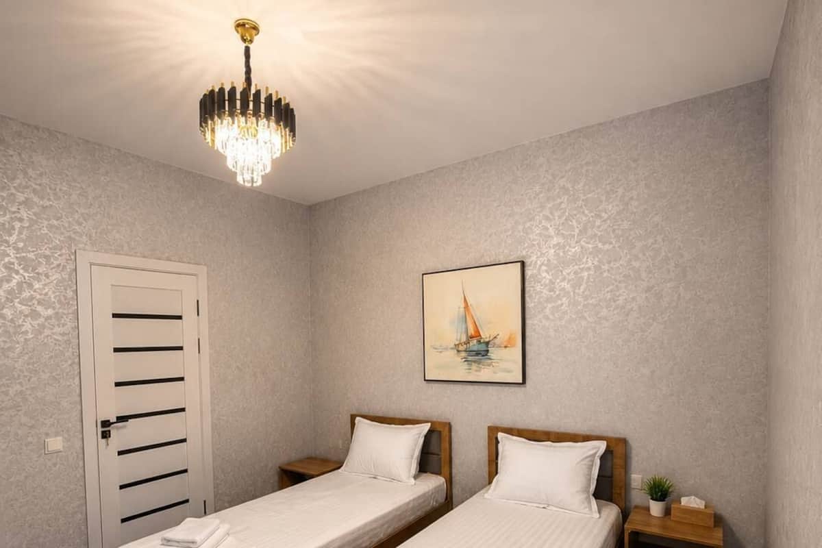 Une chambre Ă coucher avec deux lits, un lustre, un tableau, une porte et une table de chevet.
