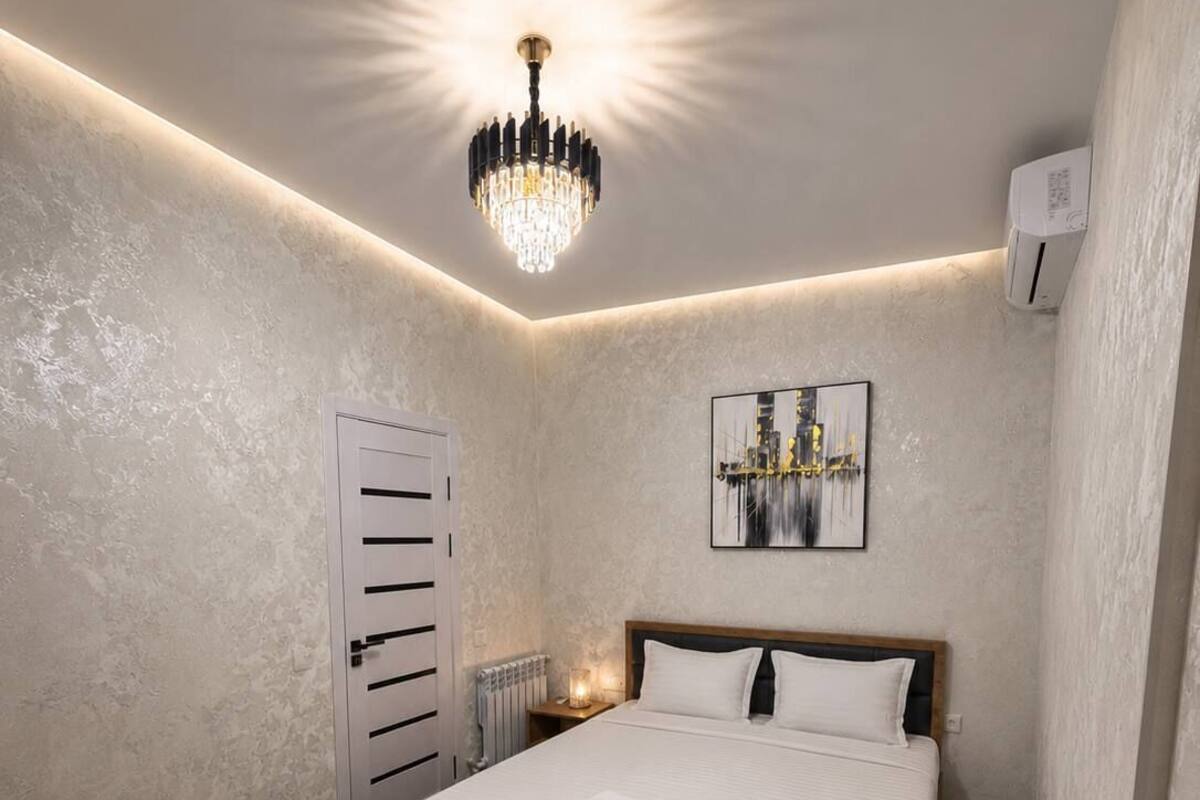 A modern bedroom with a large bed, a chandelier, a radiator, and a framed artwork on the wall.