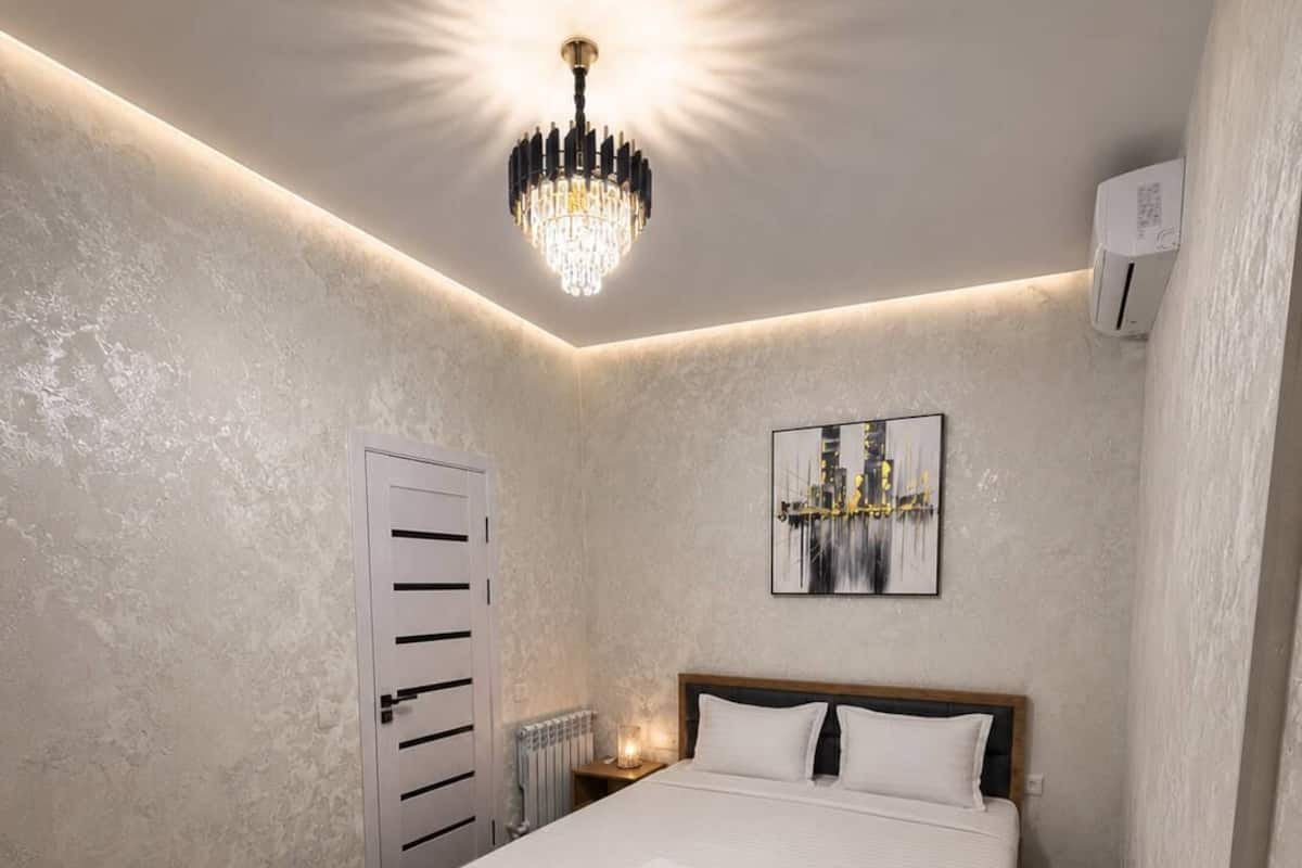 Une chambre moderne avec un grand lit, un lustre, un radiateur et une Ćuvre dâart encadrĂ©e accrochĂ©e au mur.
