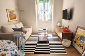 Un salon comprenant un canapé, une table basse, un téléviseur, une lampe et une fenêtre avec des rideaux.