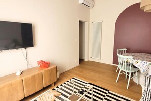 Un espace de vie moderne comprenant un téléviseur à écran plat, un banc en bois, une table à manger avec des chaises, un tapis à motifs et un radiateur.