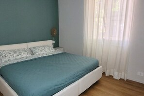 Een slaapkamer met een bed, nachtkastje, lamp en een raam met gordijnen.