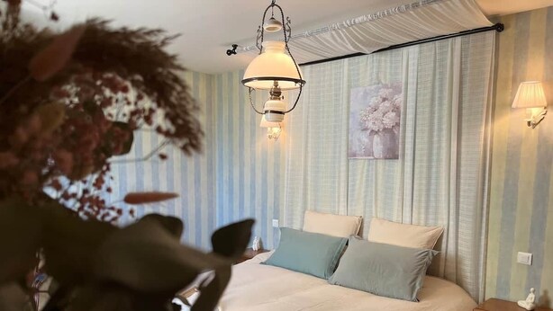 Ett sovrum med en säng, sängbord, en hängande lampa och en tavla på väggen.