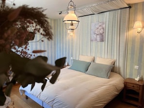 A bedroom with a bed, bedside tables, a hanging lamp, and a painting on the wall.