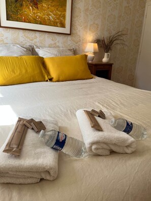 A neatly made bed with white linens, two yellow pillows, and a framed painting on the wall. - La Maison d'Odette: the Two Rooms (Saint-Rémy-du-Plain)