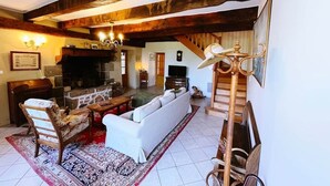 Un salon chaleureux avec une cheminée, un canapé, un fauteuil en bois et un téléviseur.