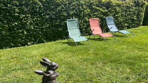 Une zone herbeuse avec trois chaises de jardin et une sculpture en pierre représentant un lapin.