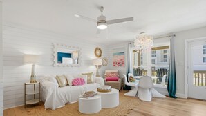 Ein Zimmer mit Deckenventilator, einer Kronleuchter, einem weißen Sofa mit dekorativen Kissen, einem runden Couchtisch und einem Korbmattenteppich.