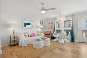 Ein Zimmer mit Deckenventilator, einer Kronleuchter, einem weißen Sofa mit dekorativen Kissen, einem runden Couchtisch und einem Korbmattenteppich.