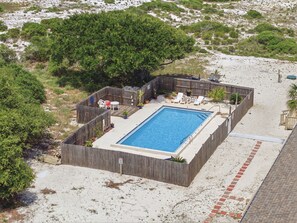 Ein rechteckiger Pool, umgeben von einem Holzzaun, mit Liegestühlen und einem kleinen Tisch.