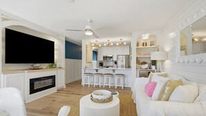 Ein modernes Wohnzimmer mit Flachbildfernseher, Kamin, rundem Couchtisch und weißem Sofa mit Kissen.