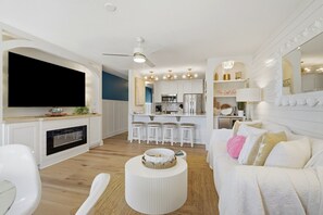 Ein modernes Wohnzimmer mit Flachbildfernseher, Kamin, rundem Couchtisch und weißem Sofa mit Kissen.