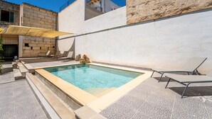 En swimmingpool med solstolar, en stenmur och en byggnad med en balkong.