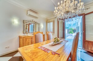 Een eetkamer met een houten tafel, stoelen, een kroonluchter en uitzicht op buiten.