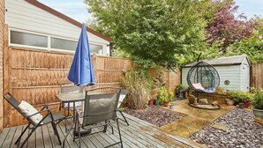 A wooden deck with a table and chairs, a hanging chair, and a garden area with potted plants and a shed. - Host & Stay | Scaife Gardens (York)
