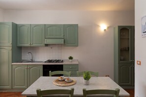 A kitchen with green cabinets, a white countertop, and a dining table with chairs. - Casa del Corbezzolo F3 by Wonderful Italy (San Teodoro)