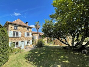 A stone building with multiple windows and shutters, a well-maintained lawn, and a large tree. - Peaceful countryside family friendly gite (6) & heated panoramic pool. (Grives)