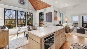 Une cuisine moderne dotée d’un grand îlot central, d’un plafond en bois et de grandes fenêtres.