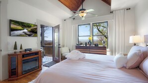 Une chambre avec un grand lit, un ventilateur de plafond, une fenêtre donnant sur un beau paysage et une armoire en bois.