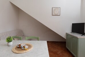 Ein Essbereich mit Tisch, Stühlen, einer Pflanze, einem gerahmten Kunstwerk und einem Fernseher auf einem Schrank.