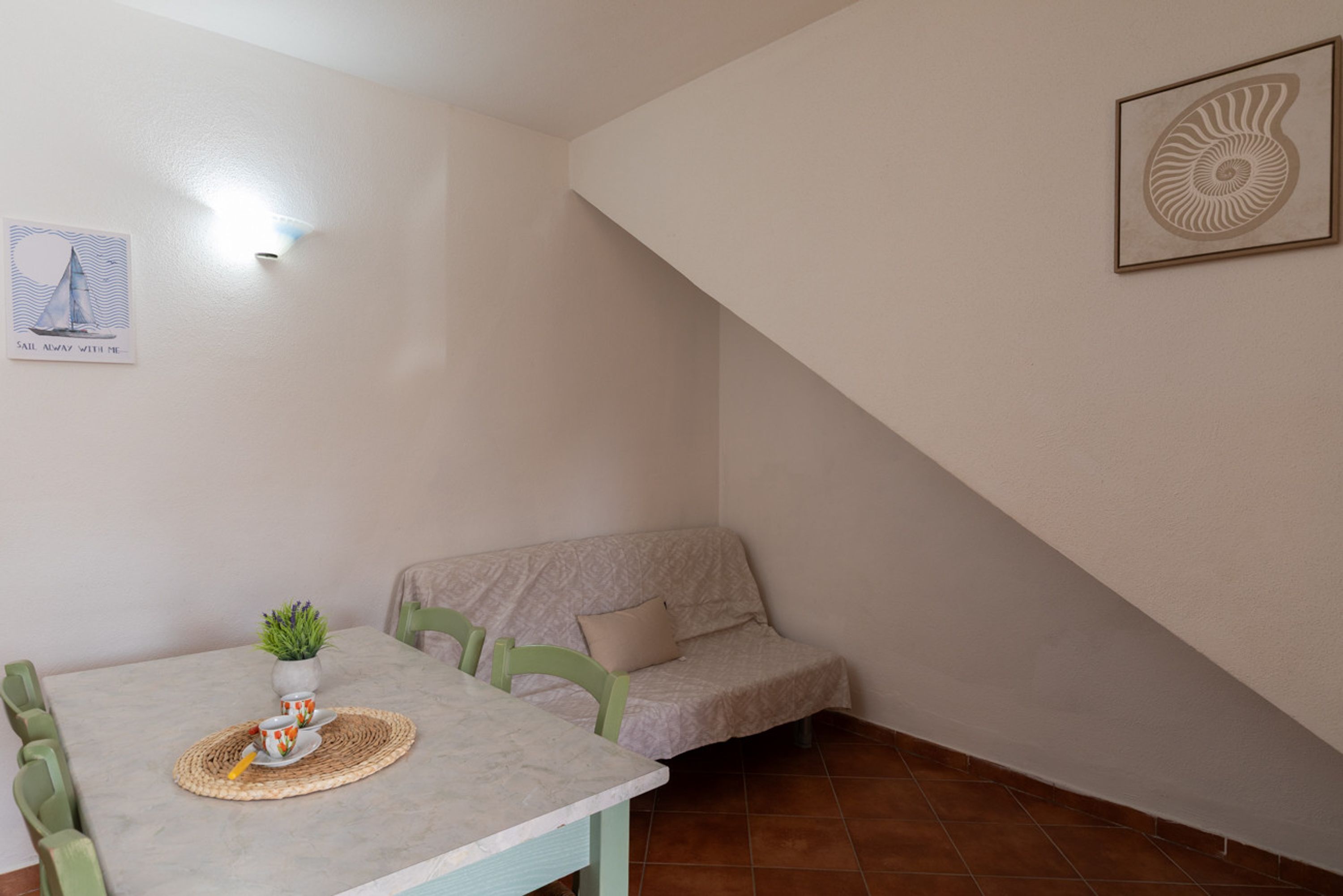 Uma área de refeições com uma mesa, cadeiras, uma pequena planta e um quadro na parede.