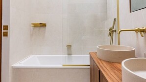 Un baño moderno con una bañera grande, dos lavamanos y una cabina de ducha con mampara de vidrio.